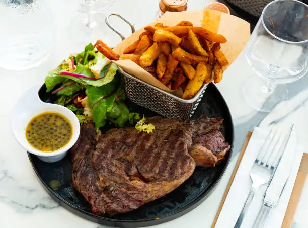 Juicy beef entrecote served with French fries, fresh greens salad and piquant lemon mustard sauce with capers
