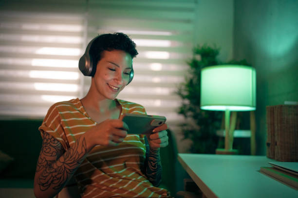 współczesna kaukaska młoda kobieta grająca w gry wideo na telefonie komórkowym - headphones music mobile phone tattoo zdjęcia i obrazy z banku zdjęć