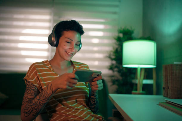 modern caucasian young woman playing video games on mobile phone - headphones women tattoo music imagens e fotografias de stock