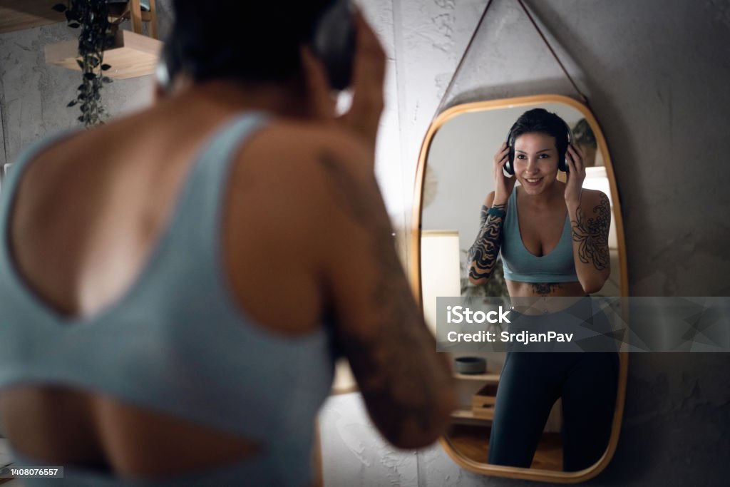 Female athlete, observing herself int he mirror, while adjusting her wireless headphones Caucasian young woman, observing herself int he mirror, while adjusting her wireless headphones 20-24 Years Stock Photo