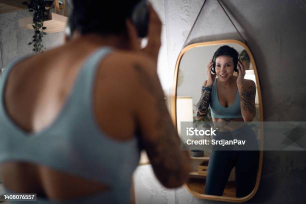 Female Athlete Observing Herself Int He Mirror While Adjusting Her Wireless Headphones Stock Photo - Download Image Now
