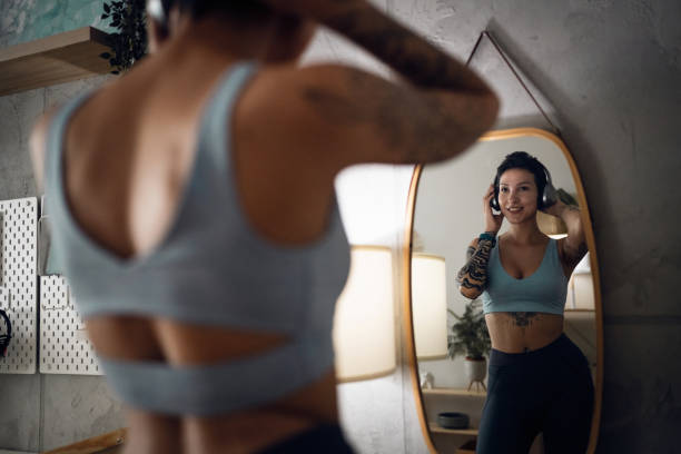 istock Female athlete, observing herself int he mirror, while adjusting her wireless headphones 1408076558