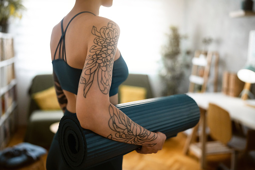 Vista lateral de una joven caucásica irreconocible con tatuajes, sosteniendo una esterilla de yoga photo