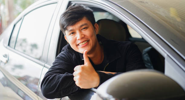 un jeune homme asiatique sourit et montre le pouce levé de la fenêtre de la voiture pour un bon service et un concept de garantie - construction safety mid adult men road construction photos et images de collection