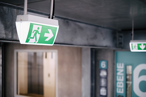 Emergency exit sign with an arrow in the direction to a door with another emergency exit sign. The sign is in a public building.