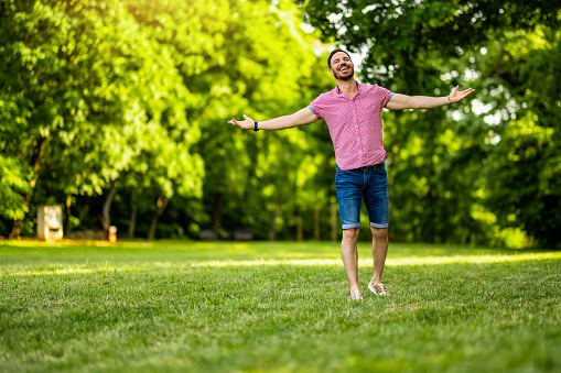 Cheerful man walking with arms outstretched in nature on beautiful summer day.