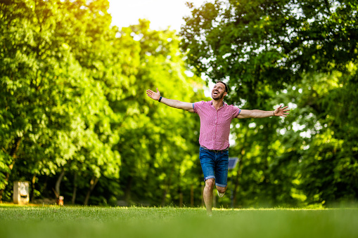 Cheerful man running with arms outstretched in nature on beautiful summer day.