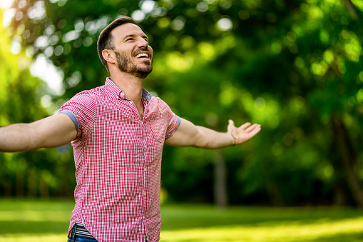 Joyful man standing while meditating with arms outstretched in nature on beautiful summer day.