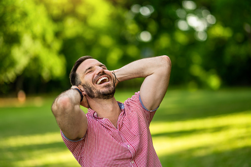 Cheerful man standing with arms behind head while relaxing in nature on beautiful sunny summer day. Copy space.