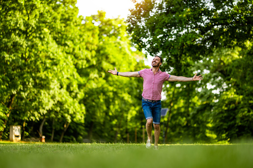 Cheerful man running with arms outstretched in nature on beautiful spring day.
