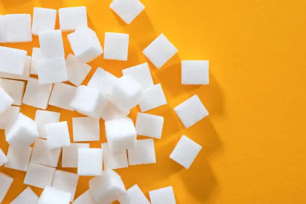 Background from sugar cubes on a yellow background. Refined sugar, top view.