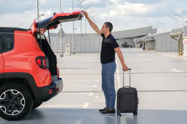 Photo of Business man taking out suitcase from car trunk