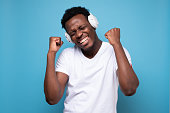 Happy emotive african man listening to music with white earphone.