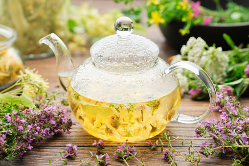 Glass tea kettle of healthy herbal tea, thyme, linden blossom, St Johns wort, yarrow, chamomile, calendula medicinal herbs on wooden table. Alternative herbal medicine.