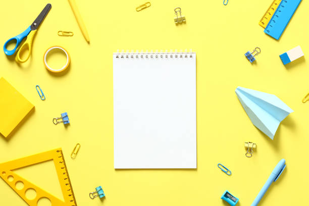 istock Blank paper notepad and school stationery on yellow table top view. Back to school concept 1408109425