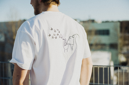 Young man with property released handmade craft designer t-shirt standing outdoors. Shot from behind, detail of the handmade custom t-shirt design. Millennial Generation Male Young Fashion Design Portrait.