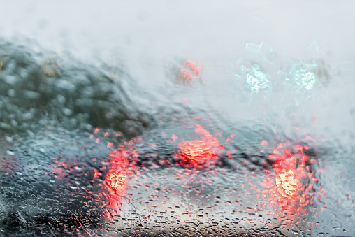 Abstract view of colorful green and red bokeh of traffic evening colors on street light background with wet rain drops on windshield dashboard of car closeup
