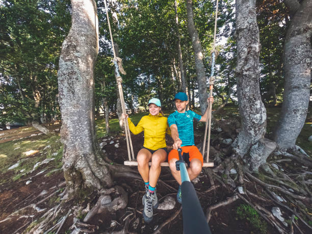 Smiling caucasian couple of hikers on a swing in the middle of a forest. Couple always searching for adventures in the nature.