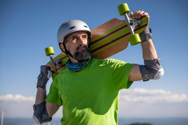 homme mûr avec longboard sur fond de ciel bleu. - senior adult outdoors wellbeing sky photos et images de collection