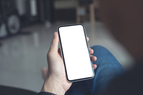 istock Mockup image of mobile smartphone with blank screen template, man sitting on sofa, hand holding and looking at mobile phone screen 1408138449