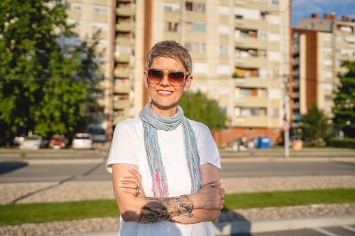 One mature woman caucasian female standing outdoor in sunny summer day wearing eyeglasses with short gray hair happy smile confident looking to the camera in the city copy space white t-shirt