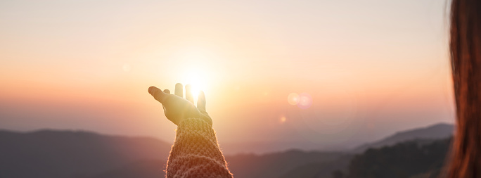 Young woman hand reaching for the mountains during sunset and beautiful landscape