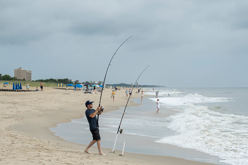 Rehoboth Beach, USA - July 3, 2022. A man fishing at Rehoboth Beach with other people enjoying their time, Delaware, USA