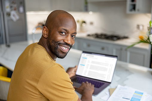Happy African American man working at home using his laptop computer and looking at the camera smiling - telecommuting concepts