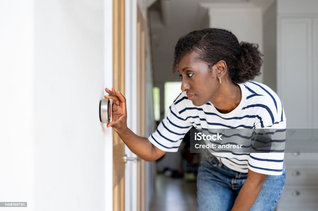 Woman adjusting the temperature on the thermostat of her house African American woman adjusting the temperature on the thermostat of her house - home automation concepts Thermostat Stock Photo