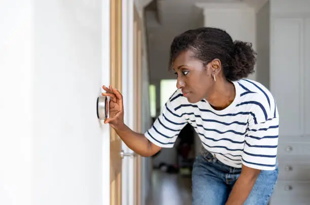 African American woman adjusting the temperature on the thermostat of her house - home automation concepts