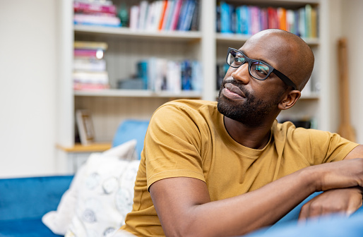 Portrait of a thoughtful black man relaxing at home on the couch while looking away wearing glasses - domestic life concepts