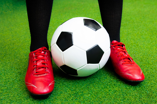 Close up football player with red soccer shoes and black and white ball on artificial grass.