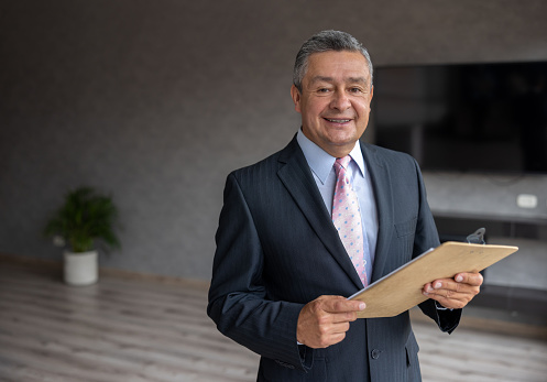 Portrait of a happy Latin American real estate agent showing an apartment and looking at the camera smiling
