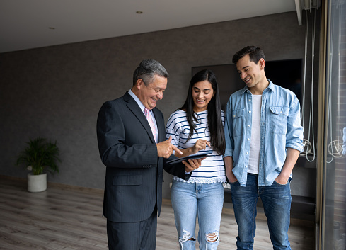 Happy couple buying a house and looking at a property with a real estate agent while smiling - home ownership concepts