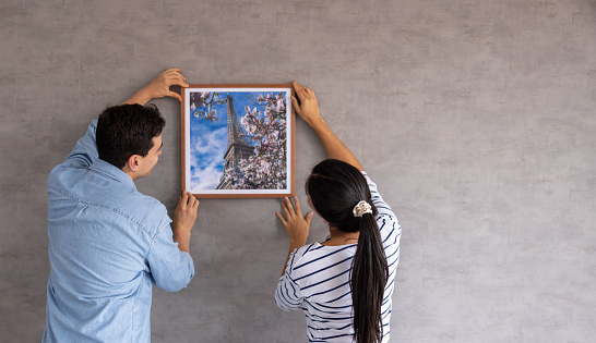 Latin American couple at home hanging a framed picture of Paris on the wall - interior design concepts