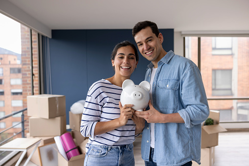 Portrait of a happy Latin American couple moving house and saving money for the future in a piggy bank