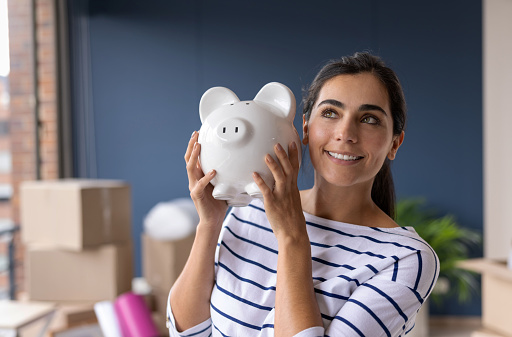 Portrait of a thoughtful woman moving house and holding a piggy bank while smiling - home finances concepts