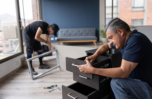 Professional movers disassembling pieces of furniture at an apartment while packing in boxes - moving house concepts