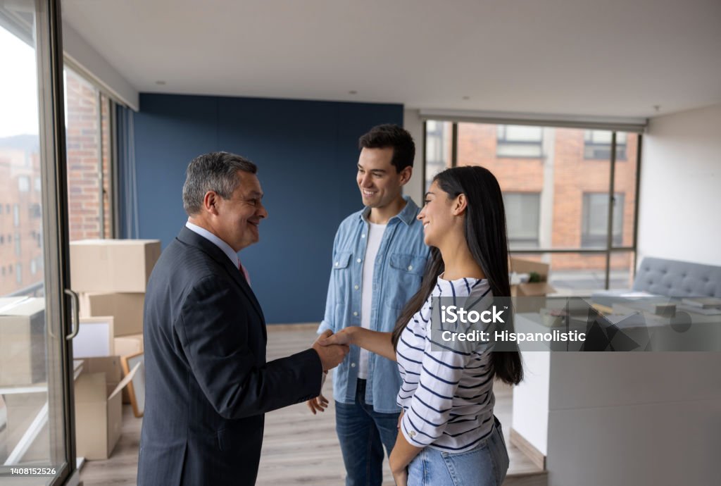 Real Estate Agent selling an apartment to a couple and closing the deal with a handshake Real Estate Agent selling an apartment to a couple and closing the deal with a handshake - real estate concepts Real Estate Agent Stock Photo