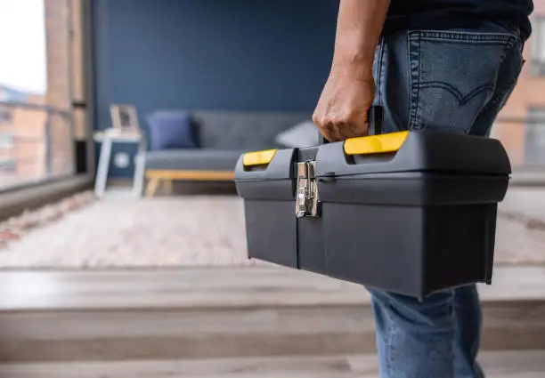 Photo of Close-up on an electrician carrying a toolbox while working at a house