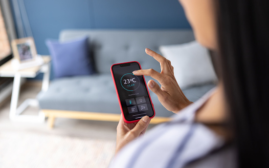 Close-up on a woman adjusting the temperature of her house using a mobile app on her cell phone - home automation concepts