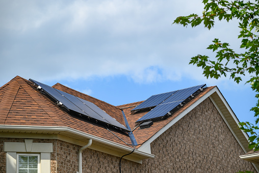 Sustainable energy - Residential solar panels installed on the roof of a house under blue skies.