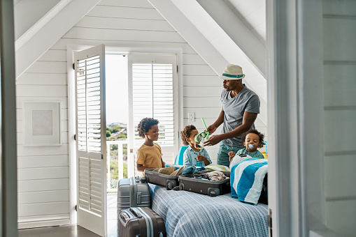 Black father on a summer vacation with his kids inside holiday a beach house. African dad preparing his children for a day at the pool. Single man nurturing his sons and taking care of them