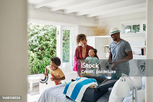 istock Cheerful black family packing for a family vacation in their home or a hotel room. Parents and two kids putting towels and toys in a suitcase for holiday by the beach. Time to travel and have fun 1408158026
