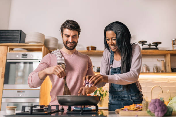 pareja multiétnica cocinando en casa - cocinando fotografías e imágenes de stock