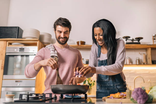 Multi-Ethnic Couple Cooking at Home Cute couple smiling and preparing lunch together in the kitchen at home. cooking stock pictures, royalty-free photos & images