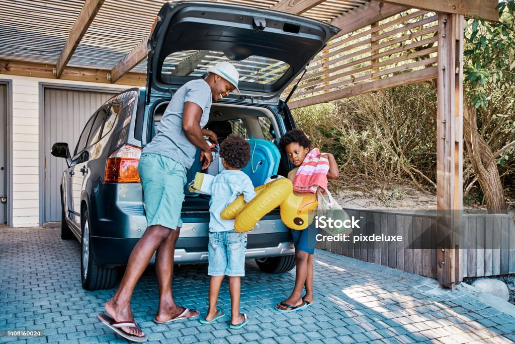 A family packing the car to leave for summer vacation. A happy african american father and his two cute little sons preparing the luggage in his vehicle to go on a road trip, ready for travel time A family packing the car to leave for summer vacation. A happy african american father and his two cute little sons preparing the luggage in his vehicle to go on a road trip, ready for holiday time Car Stock Photo