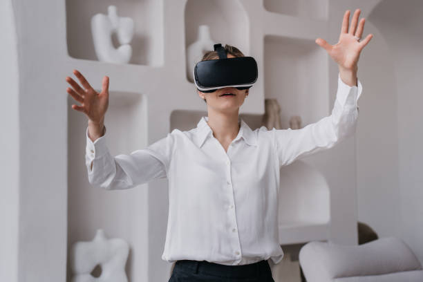 istock Young female student in white shirt and black pants using vr glasses exploring arts and museums standing indoors against wall with ceramics  on shelves. Girl using virtual reality. Education and fun. 1408160104