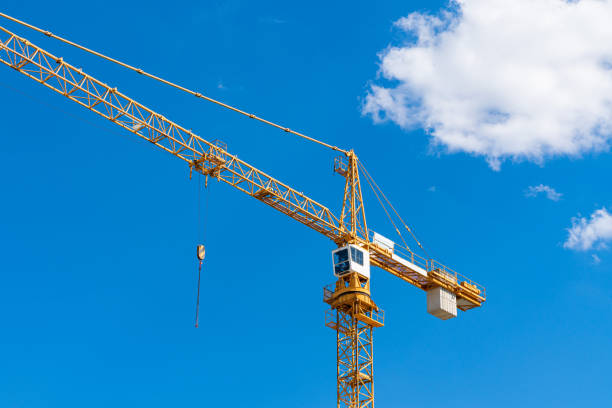 Yellow tower crane with white cab against blue sky.