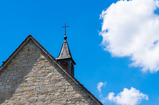 Part of the church roof with a cross against a blue sky with white clouds.